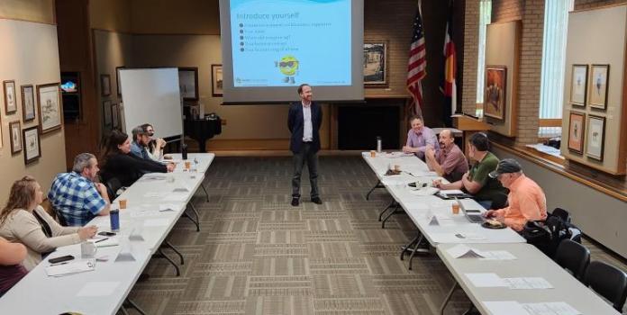 Erick Muller standing in the front of the participants sitting in a U-shaped table arrangement with a screen behind 