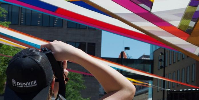 Student at Lynx Camp Denver points a camera at colorful banners in a downtown sky 