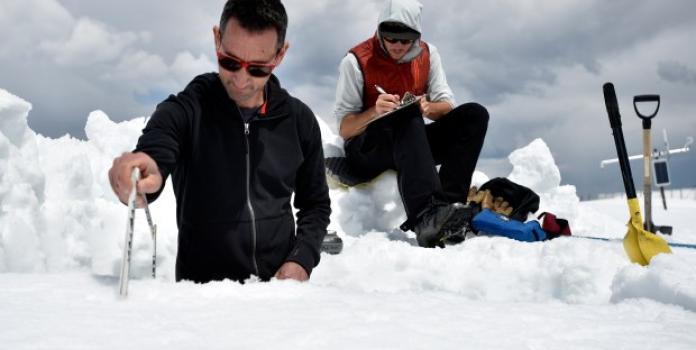 Two research students from CU Boulder take and record scientific measurements in the snow