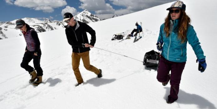 Three research students from CU Boulder walk through the snow, pulling sleds loaded with supplies.