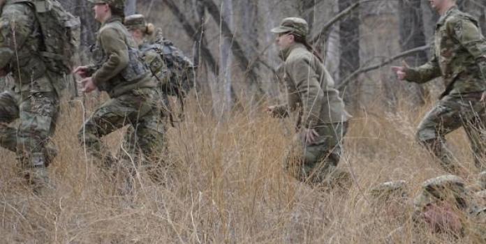 Men and women in military uniforms run through the forest