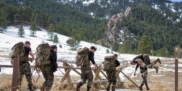 Men and women in military fatigues help each other in an obstacle race