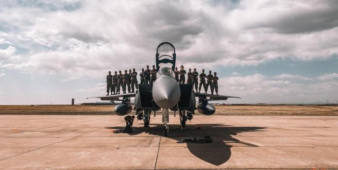 a group of people wearing military fatigues pose for a photo standing on the wings of a fighter jet