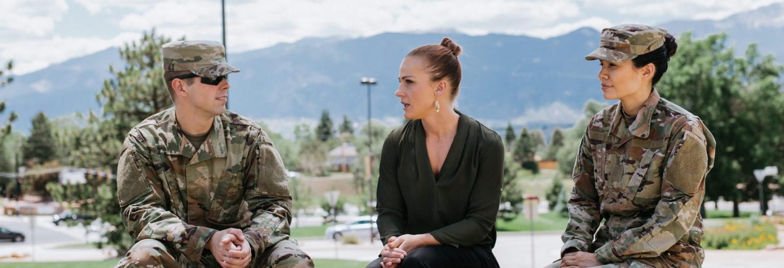 Three veterans sit outside in front of a mountain range