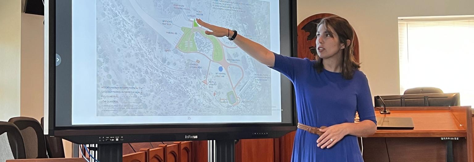 A woman points to a map on a large computer screen 