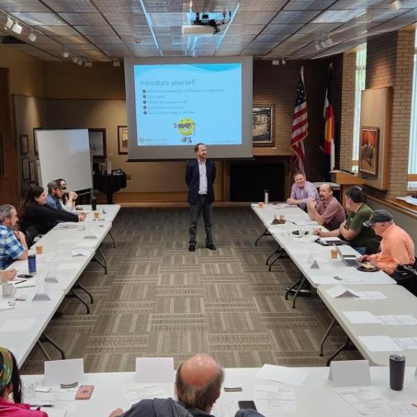 Erick Muller standing in the front of the participants sitting in a U-shaped table arrangement with a screen behind 